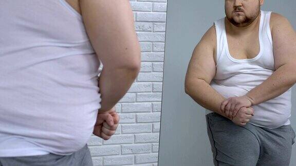 胖小伙在镜子前摆姿势假装肌肉发达、健美、正在节食