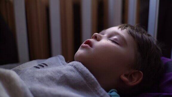 3岁小孩的特写侧视图小男孩张着嘴睡觉深呼吸在床上的毯子下躺着做梦