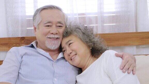 亚洲健康的爷爷坐在客厅的沙发上互相拥抱表示爱欢快的老夫妇在房子里微笑