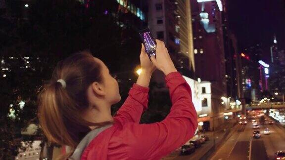 中国香港一名年轻女子在晚上用手机拍摄建筑物