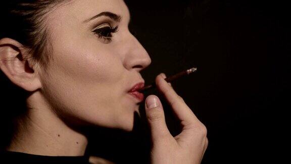一个漂亮的女人在黑色的背景上抽烟