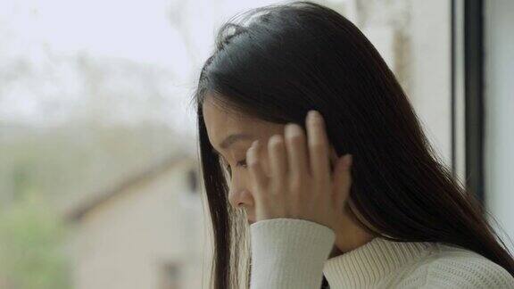 一位年轻的亚洲妇女失望地坐在房子里望着窗外