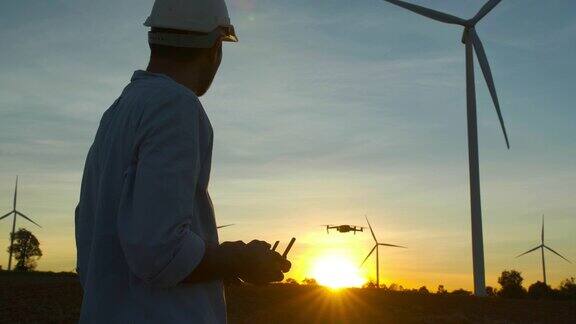 日落的剪影年轻的男性工程师控制无人机在风力发电站工作检查风力发电厂的能源生产可再生能源工厂