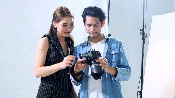 年轻的亚洲男性摄影师展示照片给女模特在相机显示手持拍摄