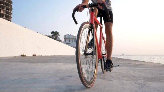 年轻人骑着他的固定齿轮自行车在海滨日落或日出