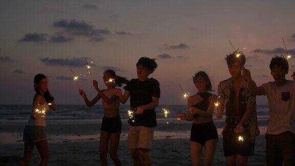 一群朋友在海边的夜晚聚会上玩的孟加拉灯在他们的手青少年们在海滩上用烟花聚会慢动作镜头