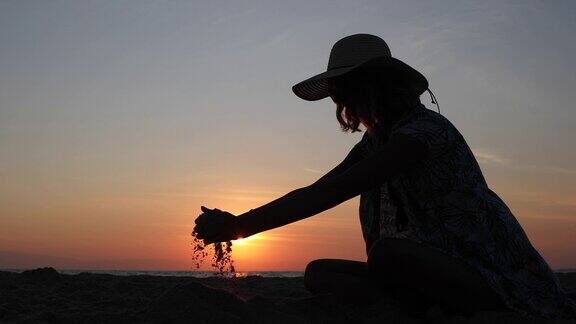 年轻女子在沙滩上玩沙子美丽的夕阳为背景