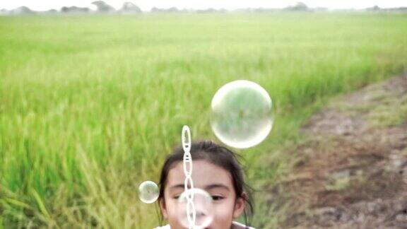 亚洲的孩子们笑着在一个夏天的绿色稻田吹泡泡与慢动作股票视频有乐趣