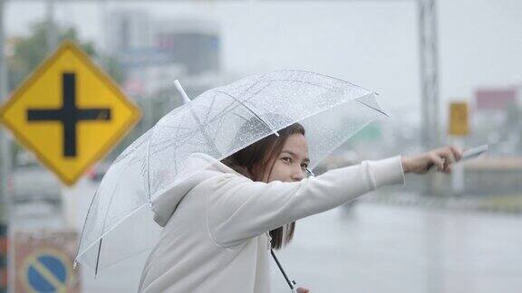 一个亚洲女人撑着伞在雨天的城市街道上搭出租车