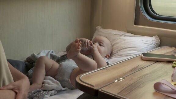 母子俩乘火车旅行火车车厢里6个月大的可爱男婴在靠窗的座位上喝奶瓶里的奶