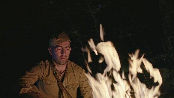 一个悲伤孤独的二战士兵坐在树林里的火旁悲伤地看着火