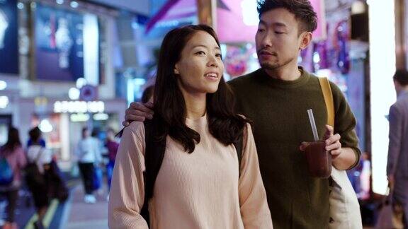 SLOMO手持式中景:一对年轻夫妇在夜晚穿过香港