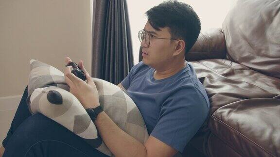 年轻的亚洲男人在家里的客厅里玩电子游戏集中的亚洲人在现代客厅玩操纵杆