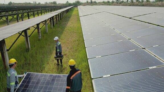 工人手持太阳能电池板在太阳能农场行走的俯视图工程师检查太阳能电池板的构造无人机飞行飞越太阳能电池板领域的可再生绿色替代能源