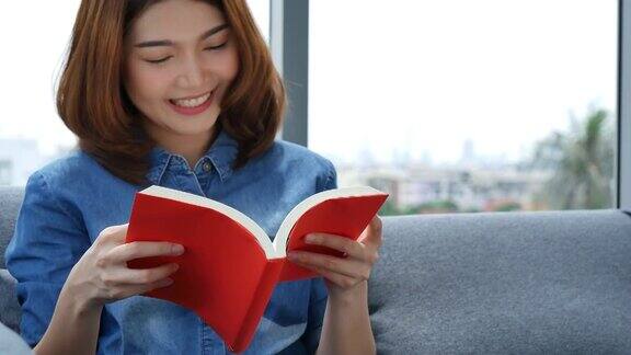 年轻的亚洲女人在温暖的家舒适的沙发上看书放松女人拿着书在靠近窗户的沙发上看幸福女人读书开书闲心幸福女人生活在家里