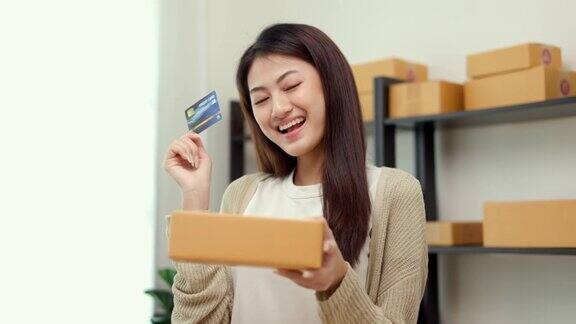 微笑的亚洲妇女网上购物展示信用卡和包裹盒女性在网上用支付方式购买商品感觉在家就很开心