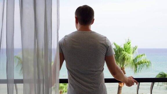 度假的男人拉开窗帘走到阳台上从阳台上欣赏地中海的海景