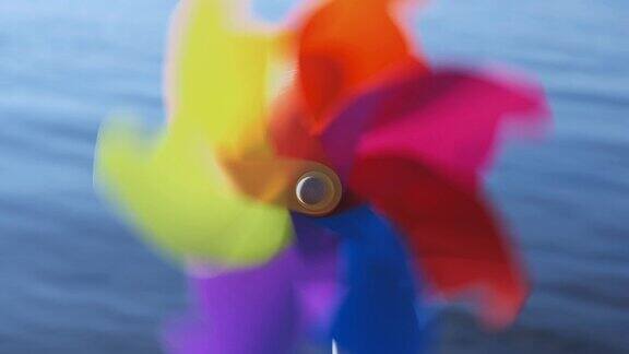 随着风的吹动在海边的沙滩上旋转着彩色的塑料风车映衬着蓝色光滑的海面和一天的日落海滩上的玩具工厂Copyspace模式