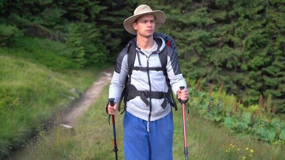 千禧年旅行者的肖像男游客拿着登山杖和背包从森林中走出来在山间徒步旅行旅游