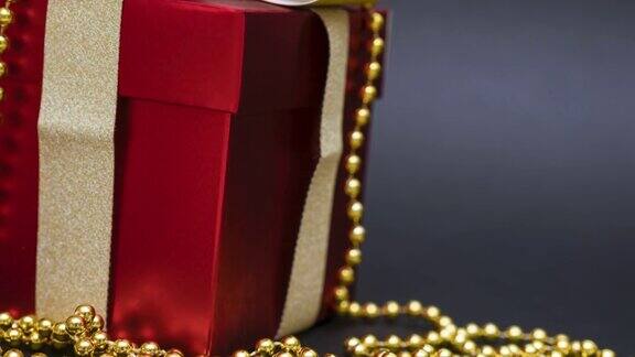漂亮的红色礼品盒黑色背景上有一个金色的蝴蝶结和珠子