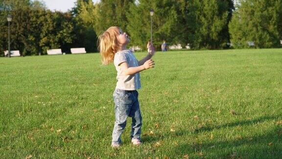 一个快乐的小女孩在夏日公园的草坪上跑步玩黄色的足球扔和接球