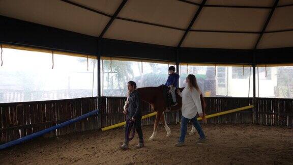 女教练牵着一匹马带着一个孤独症孩子