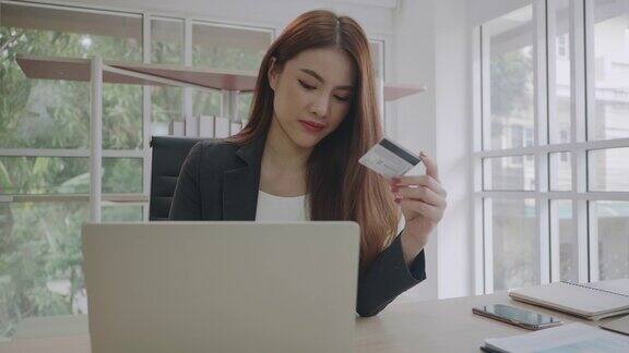 美丽的年轻亚洲女商人在办公室用她的笔记本电脑在网上购物