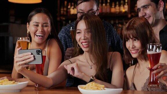 年轻的亚洲朋友在酒吧喝酒看着相机自拍微笑