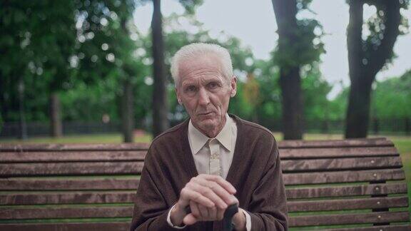 心烦意乱满脸皱纹的老人独自坐在城市公园里手里拿着拐杖