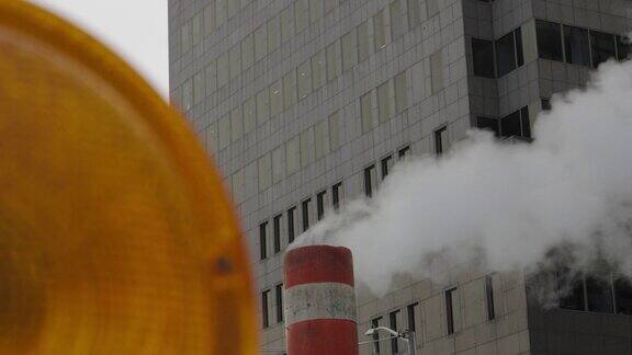 蒸汽从施工管道中喷出前景是警示灯背景是城市办公大楼