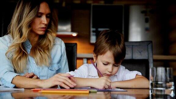 美丽的妈妈帮助她的儿子用彩色铅笔画图像帮助发展孩子的想象力
