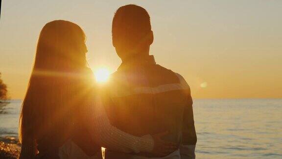 年轻的多民族情侣在日落时拥抱站在海边白人女人和亚洲男人