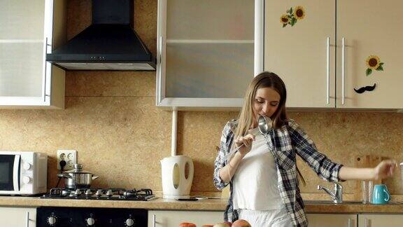 欢快的年轻有趣的女人在厨房做饭的时候用勺子跳舞唱歌的慢动作