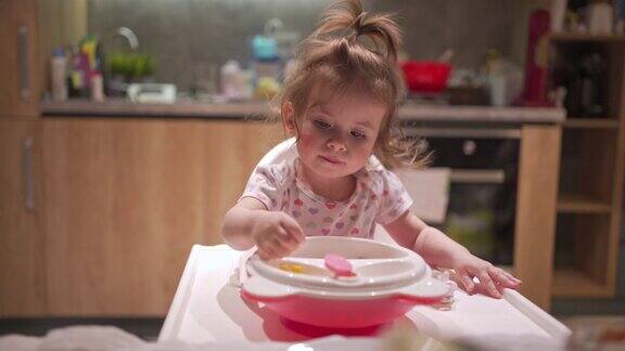 可爱的小女孩脸蛋红润在高脚椅上吃饭的时候玩着食碗