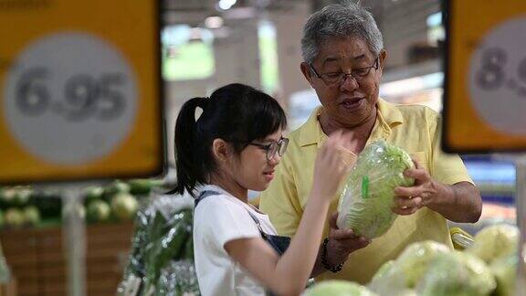 一个活跃的亚洲华人老人和他的孙女在购物和挑选白菜