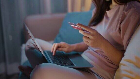 年轻女子高兴地在沙发上用信用卡订购网上购物产品