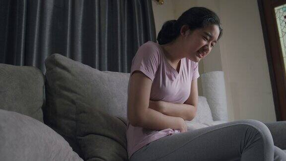 亚洲少女有盆腔疼痛胃痛而坐在家里的沙发上