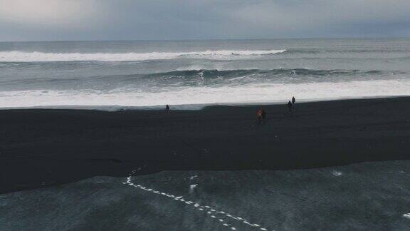 在冰岛的火山黑沙滩上散步和在日落时玩耍的朋友的无人机视图海滩上的人们