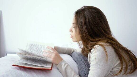 快乐的年轻女人在家里卧室的床上看书