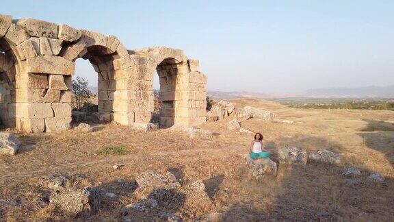 日落时分一个美丽的女人在老底嘉古城的废墟上冥想做瑜伽