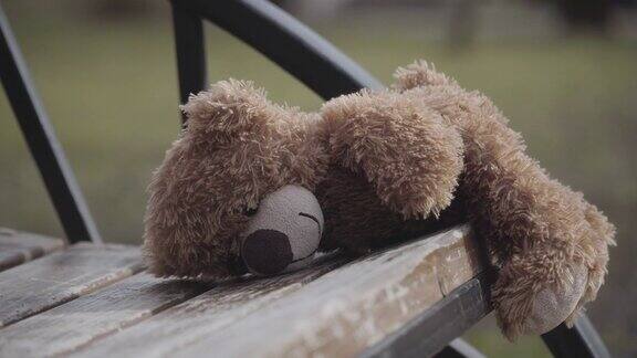 泰迪熊躺在城市公园的木凳上的特写失去了户外玩具孤独被遗弃绑架走失的孩子