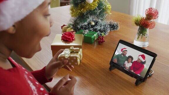 戴着圣诞帽的非裔美国妇女使用平板电脑与屏幕上的家人进行圣诞视频通话