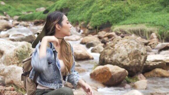 4K亚洲女人坐在小溪边的岩石上
