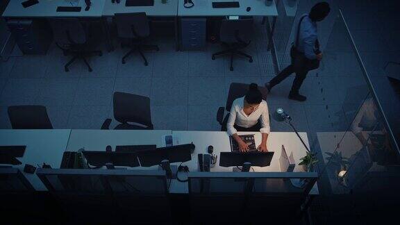 在办公室工作到深夜:女商人使用台式电脑分析使用文件解决问题完成项目同事说再见然后离开高角度拍摄
