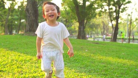 高清:快乐的小男孩在公园里奔跑背景是夕阳(慢镜头)