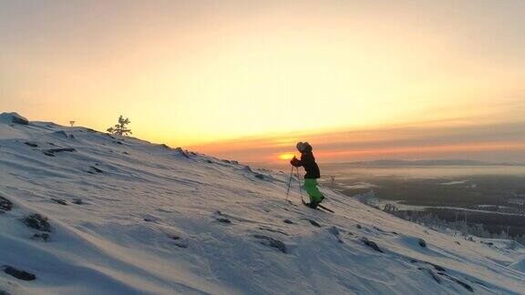 在金色的日出中一名年轻女子穿着雪鞋向山顶攀登