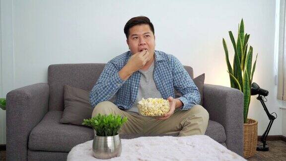 4k视频的亚洲人看电视喜剧电影或体育和吃爆米花享受在家里的沙发上