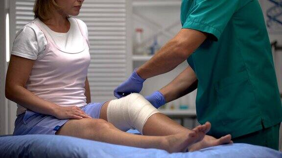男医生在女性患者膝盖上应用弹性包进行创伤康复