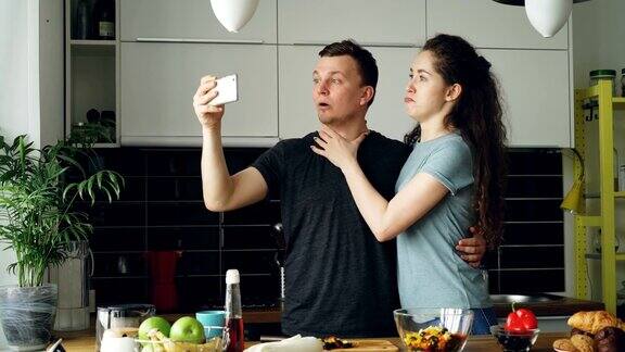这对年轻有趣的情侣早上在家厨房做饭的时候用智能手机自拍