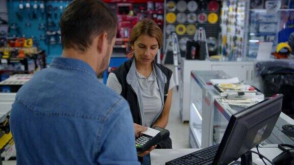 在五金店愉快的女售货员正在为用信用卡付款的顾客办理付款手续